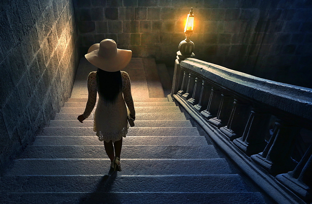 Woman in white lace dress and hat walking down stairs on colonial staircase in San Agustin Church, Manila, Philippines