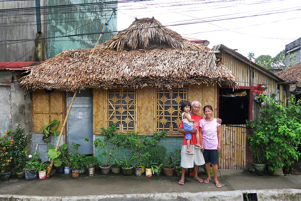 Portrait of grandparents with child looking at camera outside straw hut, Legazpi City, Albay Province, Philippines