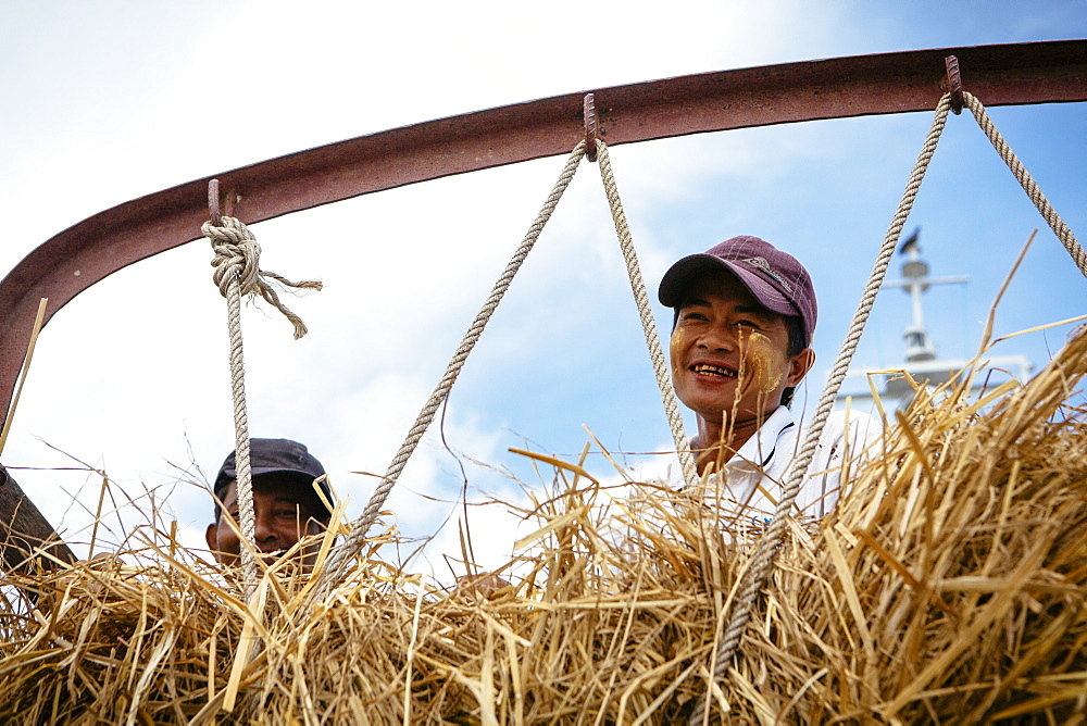 Farmers look out over the side of a hay truck as they cross a river, Yangon, Myanmar