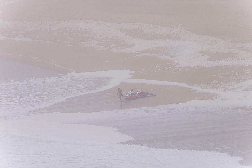 Man in fife jacket leading rescue jet ski in water at beach of Praia Norte, Nazare, Leiria, Portugal