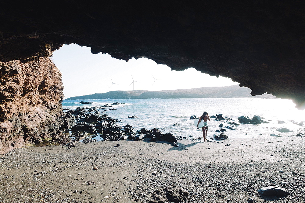 View from cave of female surfer in bikini walking with her surfboard on beach, Tenerife, Canary Islands, Spain