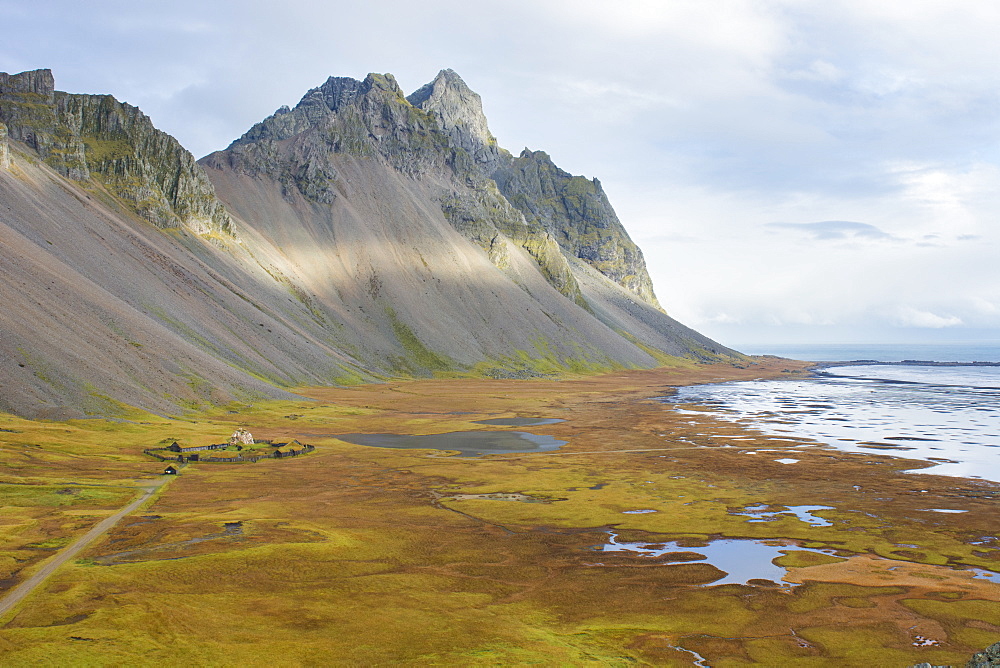 An elevated view of Stokksnes beach, with its movie set Viking village in the middle, green and orange autumn colors, the ocean and the mountains Vesturhorn and Vestrahorn, Stokksnes, East Iceland, Iceland