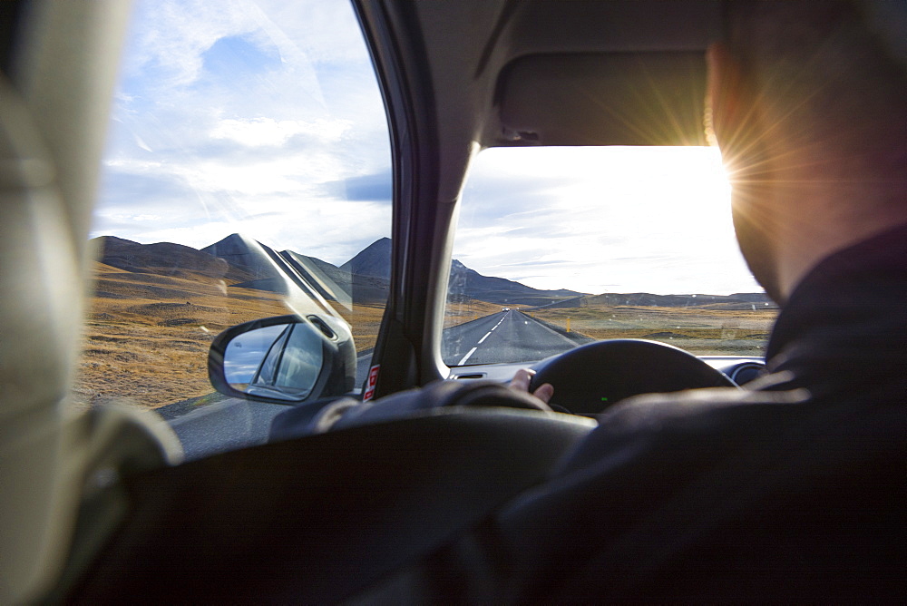 An over the shoulder viw of a young man driving the Ring Road as the sun begins to set, in North Iceland.