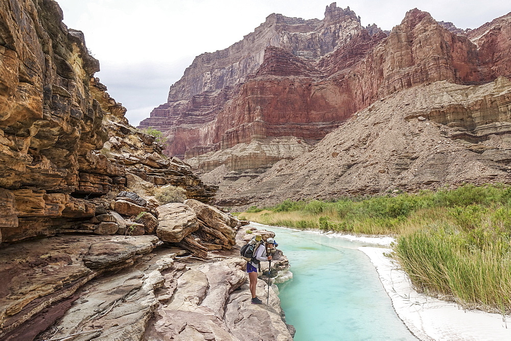 Landscape with young woman standing on rock formation and contemplatingÂ turquoise water of Little Colorado River near its confluence with Colorado deep down in Grand Canyon, Grand Canyon, Arizona, USA