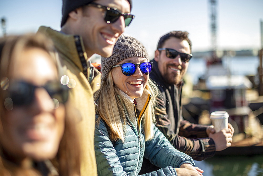 Portrait of young woman wearing sunglasses laughing while waiting with friends at harbor, Portland, Maine, USA