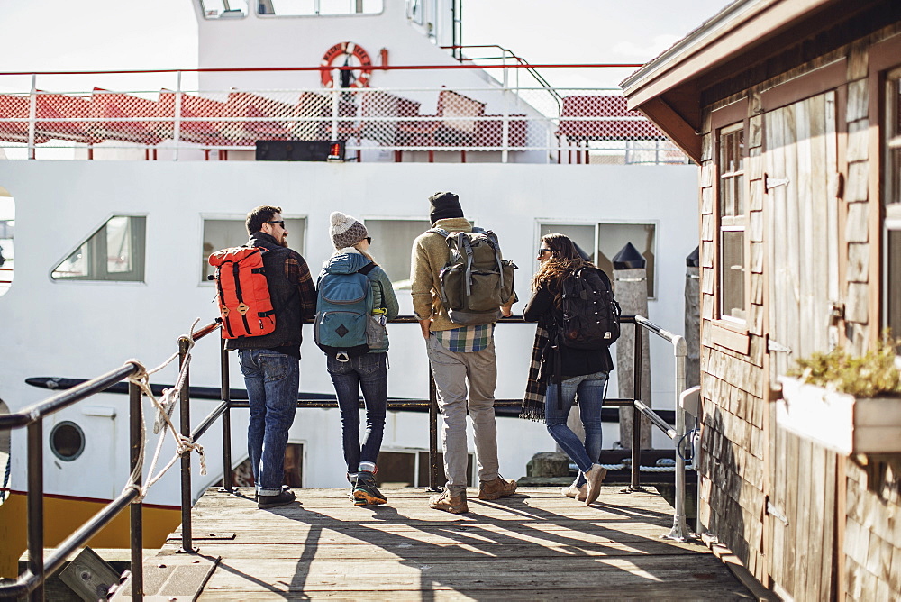 Four adult friends waiting with backpacks for ferry, Portland, Maine, USA