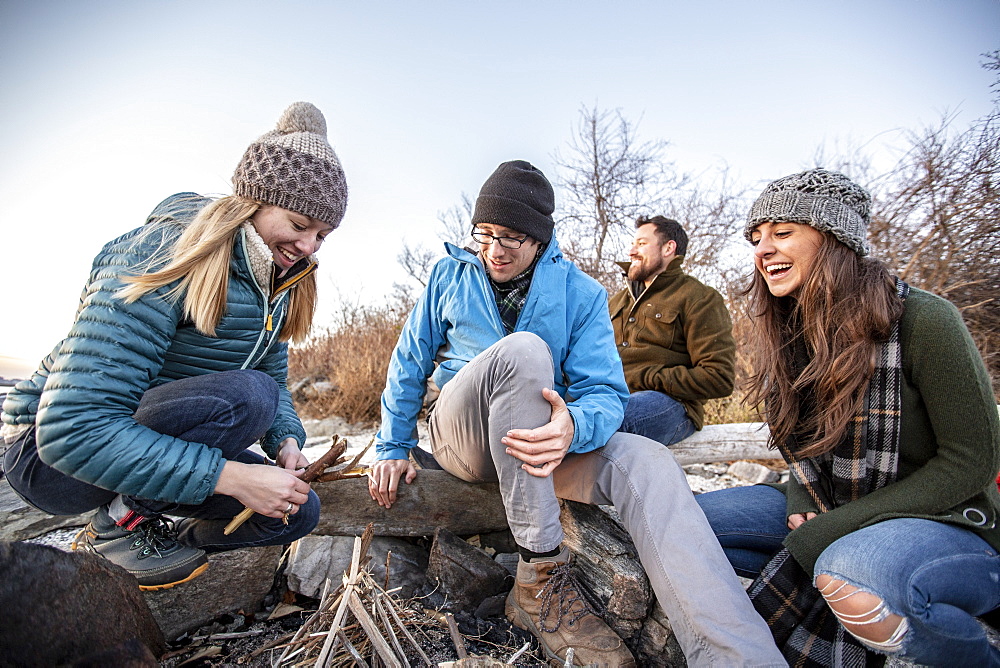 Four adult friends preparing campfire on coastal beach in autumn, Portland, Maine, USA