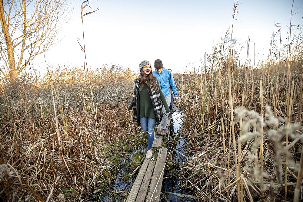 Young couple crossing narrow boardwalk during hikeÂ through tall grass, Portland, Maine, USA