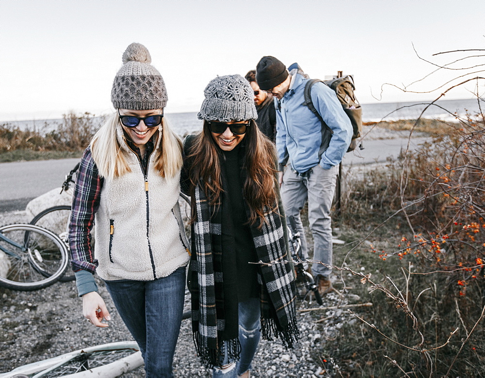 Group of adult friends leaving bicycles and walking beside bushes during hike, Portland, Maine, USA