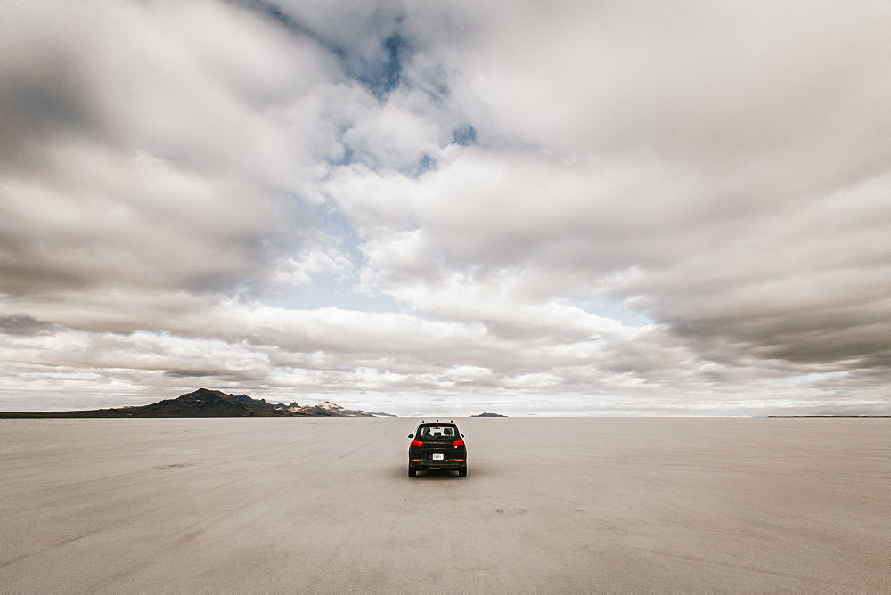 Lone car driving along expansive desolate Salt Flats, Â Wendover, Utah, USA