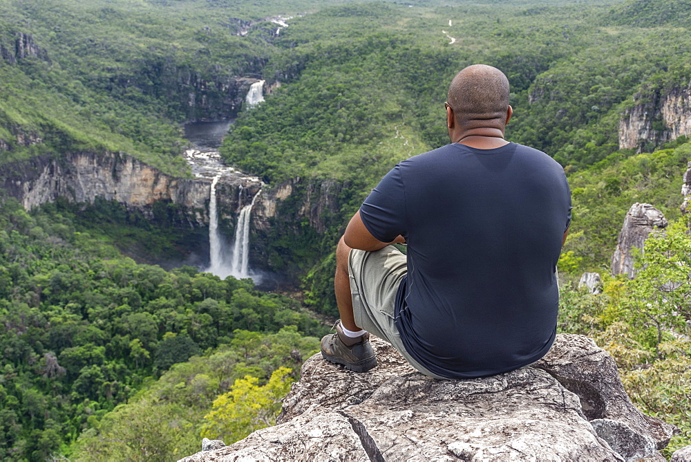 Mid adult man sitting on rocky edge with beautiful natural cerrado landscape on the background, Mirante da Janela hike, Chapada dos Veadeiros, Goias, central Brazil