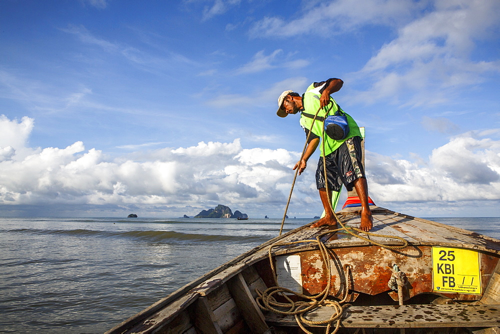 A boat captain raises the anchor on a boat along that coast of Krabi, Thailand before a ride to Railay Beach, a popular tourist destination.