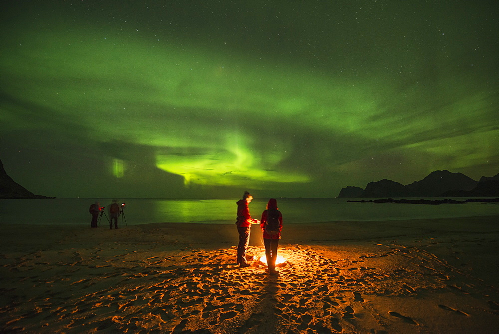 Tranquil scene with people around campfire on beach under aurora?borealis?at night, Flakstadoya, Lofoten Islands, Norway