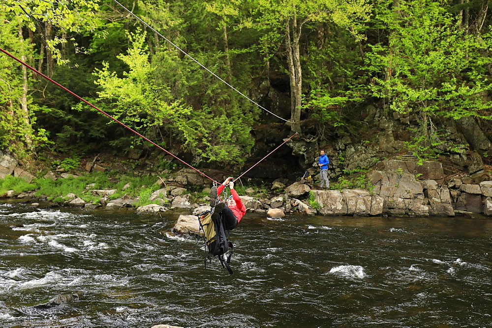 Climber traversing across the Au Sable River to access the climbing a route on Moss Cliff above Wilmington Notch, Adirondack Mountains, New York State, USA