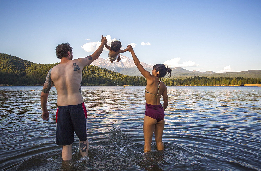 Rear view of couple in swimsuits playing with baby daughter in Lake Siskiyou, California, USA