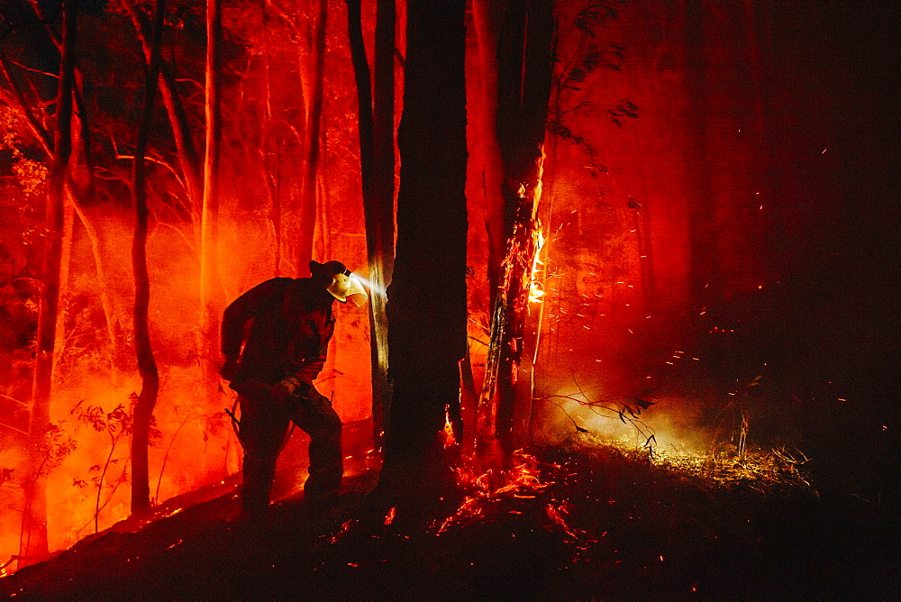 Firefighter using a backpack to extinguish hot spots near the containment line, Guanaba, Queensland, Australia.