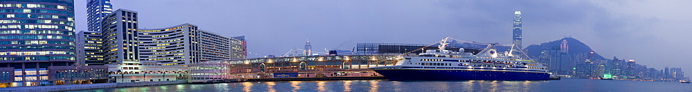 Night time view of a cruise ship docked at Tain Sha Tsui, Kowloon, with the buildings of central Hong Kong visible in the background, Hong Kong, China.