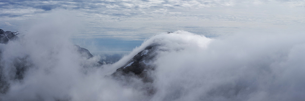 Low clouds conceal mountains and fjords from summit of Volandstind mountain peak, Flakstadøy, Lofoten Islands, Norway