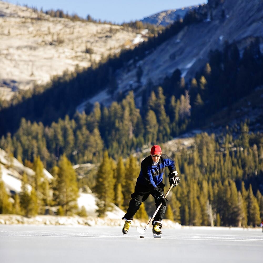 Low angle front view of a ice skater playing ice hockey on a snow free, frozen Tenaya Lake in Yosemite National Park.