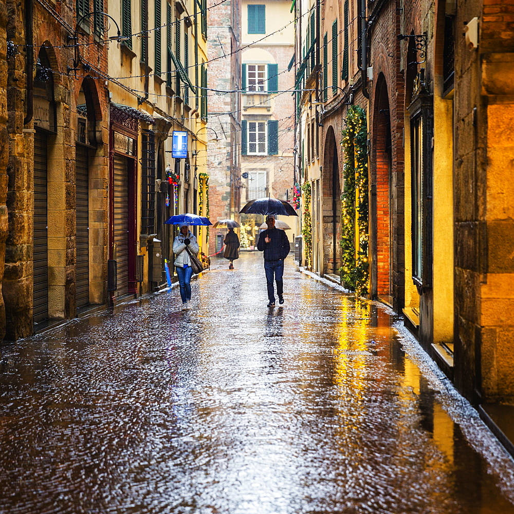 People walking the wet city streets in Lucca, a city and commune in Tuscany, Central Italy, on the Serchio, a fertile plain near the Tyrrhenian Sea. It is the capital of the Province of Lucca. It is famous for its intact Renaissance-era city walls.