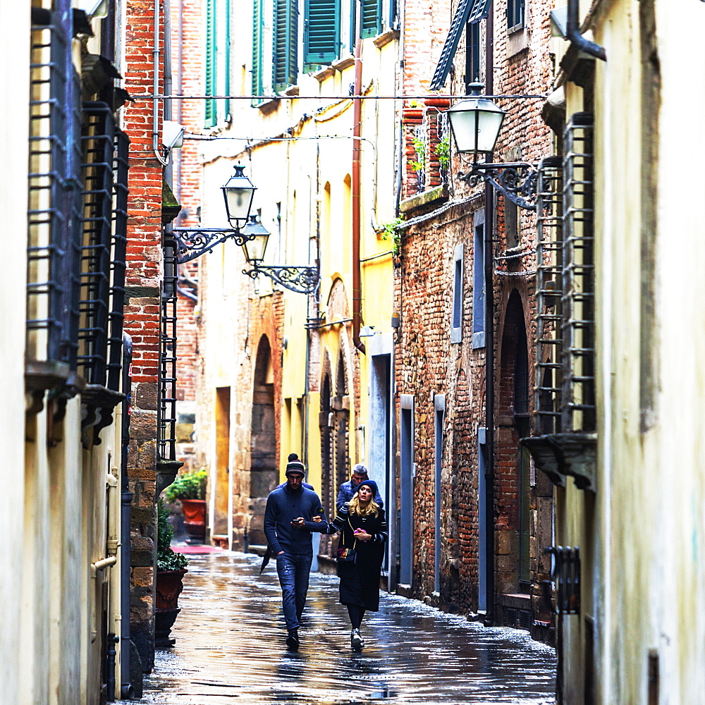 Front view of people walking the wet city streets in Lucca, a city and commune in Tuscany, Central Italy, on the Serchio, a fertile plain near the Tyrrhenian Sea. It is the capital of the Province of Lucca. It is famous for its intact Renaissance-era city walls.