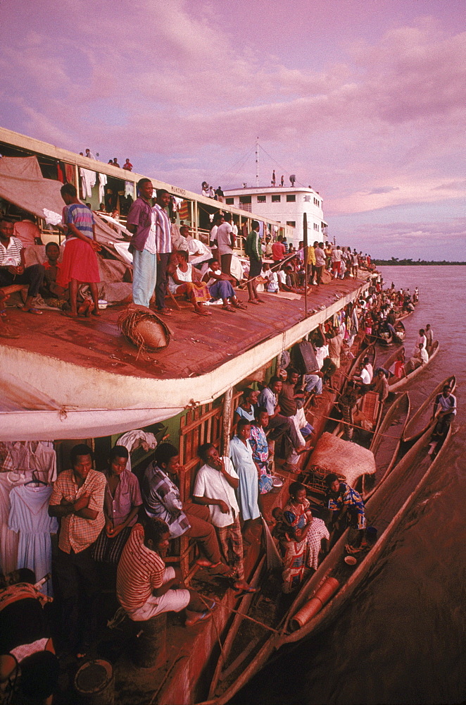 View of one of the crowded barges and the dugout canoes or pirogues which the fishermen and hunters who live along the Congo River use to bring bush meat to the boat to trade for salt, sugar and other goods.