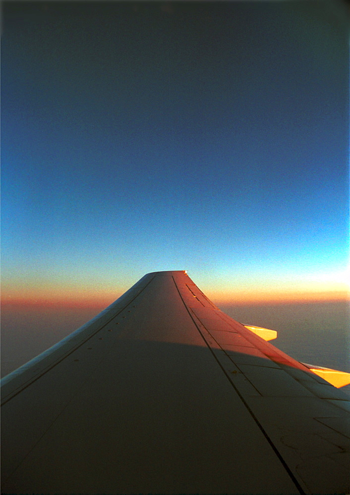 An airplane wing against the horizon while flying during sunset.