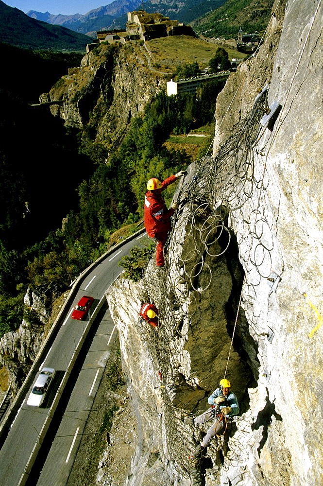 After the helicopter has put the net into place the workers fasten the loose boulder to the cliff.