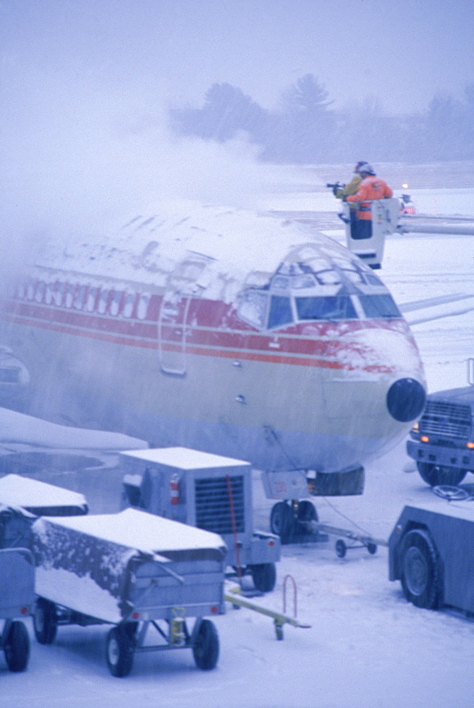 Men de-icying top of jet during snow storm at Portland International Jetport, Portland, Maine