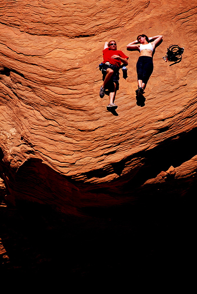 Tim Burnett and Leslie Barber resting on a flat santstone table while watching friends rock climbing on a sandstone cliff high above Lake Powell, Utah. Burnett and Barber were on a houseboat climbing expedition. The team of climbers used the houseboat as a base camp and a small speed boat to explore the many great sandstone cliffs that surround the lake.