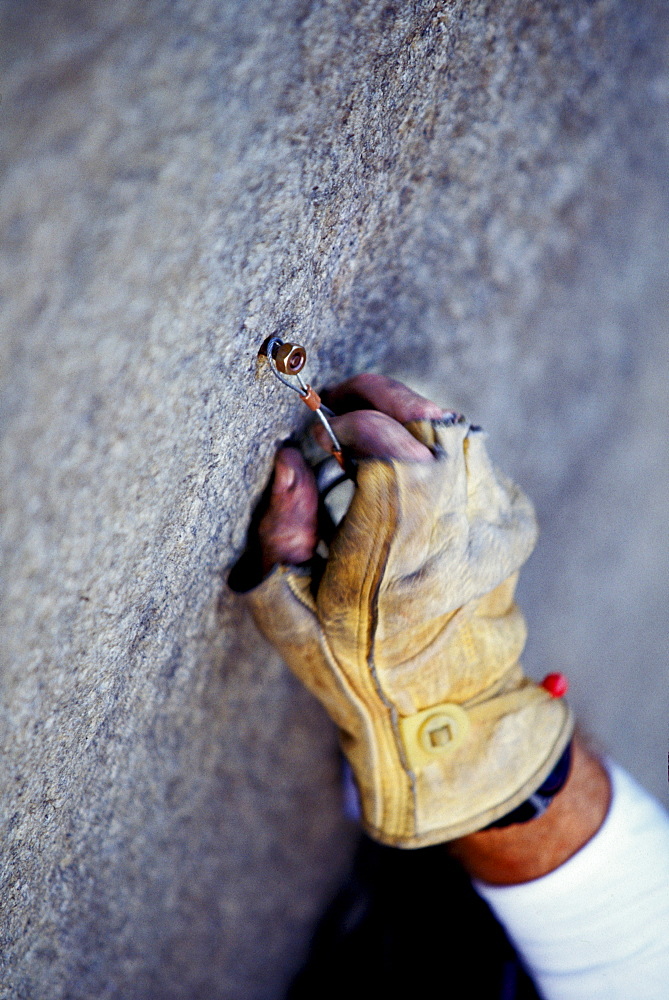 Martian Avidan rock climbing, aid climbing, big wall climbing up the Zodiac 5.13+ on El Capitan in Yosemite National Park, California. In the photo you see Avidan placing a wire rivet hanger on a rivet. The climber wears leather gloves to protect his skin from the elements. The team spent three days and two nights on the big wall. Several haul bags are visible in the photo.