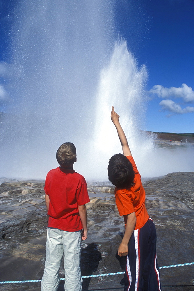 An Icelandic boy and an American boy watch the Strokkur Geyser erupt at Geysir, Iceland.