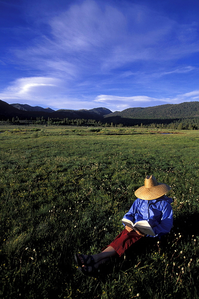 Nina Schmalenberger reads a book while camping in Hope Valley near Lake Tahoe, California, in the Sierra Nevada Mountains. She is wearing a straw hat.