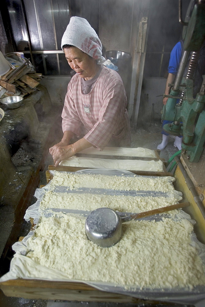 Kazuko Uezu, age 65, makes tofu before dawn in her small shop in the village of Hedo.  Despite 50 years of practice "every batch tastes slightly different" says Kazuko who rises at 4-am seven days a week to make tofu.  Traditional methods and a small production produces subtle variations in every batch despite the fact that tofu has only two ingredients, salt water and soy beans.  Kazuko get the salt water from the East China Sea (just down the road from her house) but the soybeans come from America.  Okinawan centenarians eat tofu daily and it is believed the high flavanoid content in tofu contributes to their longevity.  Flavanoids are known to fight breast and prostate cancer and believed to combat heart disease.