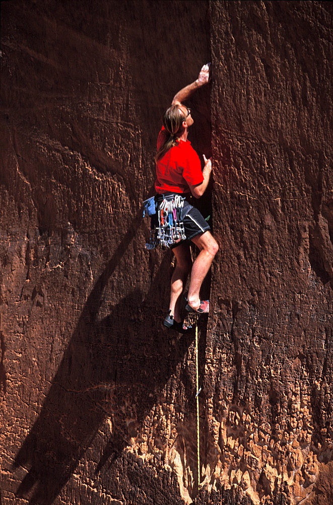 Tim Burnett looking to place a cam somewhere in the crack he is climbing in Lake Powell, Utah.