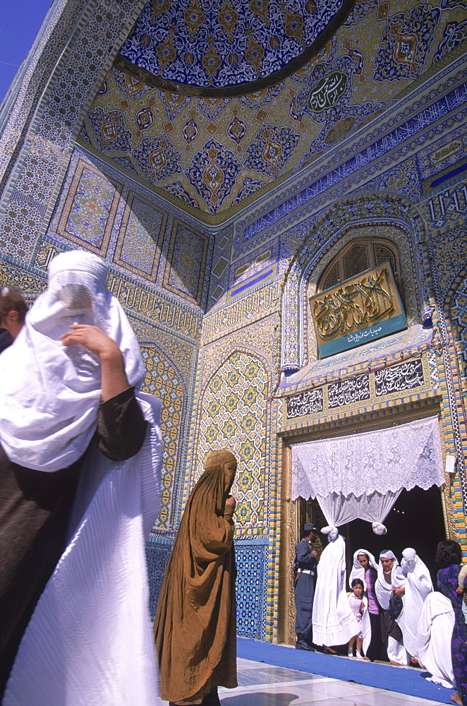 Women in burqas flock like doves to the entrance of the main mosque at the Blue Mosque complex, Mazar-i-Sharif, Balkh Province, September 23, 2002.  Wednesday mornings are reserved for women to come and worship at the mosque.Elaborate tilework and decorated spires adorn the mosque, also known as the Shrine of Hazrat Ali (Hazrat Ali was the son-in-law of the prophet Mohammed), who is believed to be buried here.  The shrine, of particular importance for Afghanistan's Shi'ite Muslims, was first built in the 12th century, destroyed by Genghis Khan, and rebuilt in 1481.  The current mosque, considered by some to be one of the most beautiful in Central Asia, is a modern restoration.