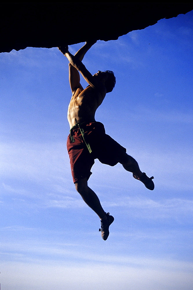 Adam Wanden in an afternoon bouldering session on a highball roof problem framed agains the sky.