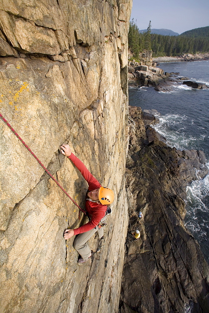 A man rock climbing on oceanside cliffs in Acadia Nation Park.