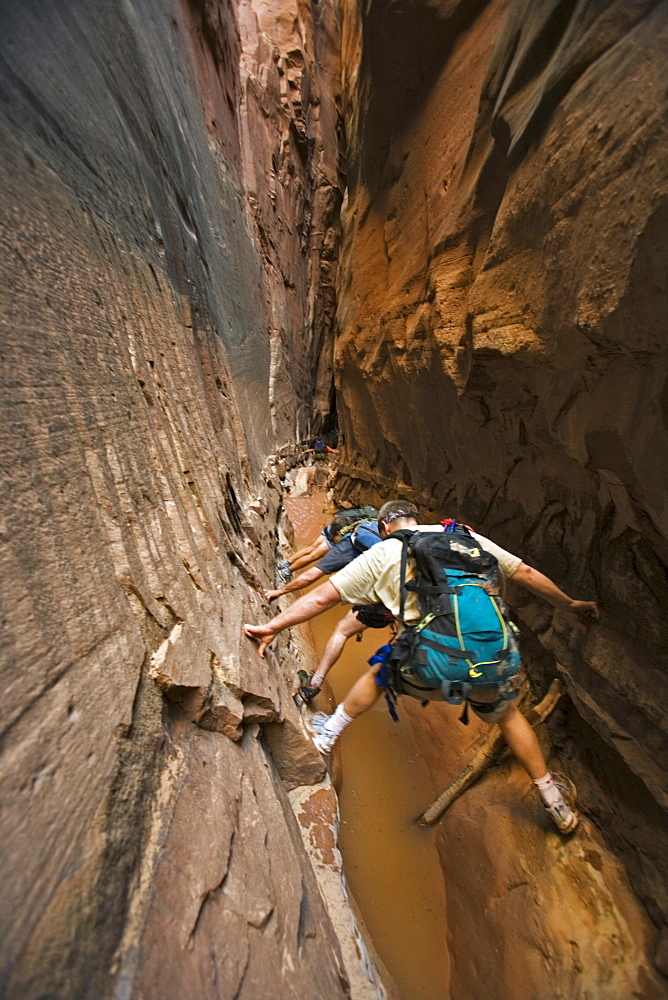 Three people stemming between two walls above water in slot canyon, Utah.