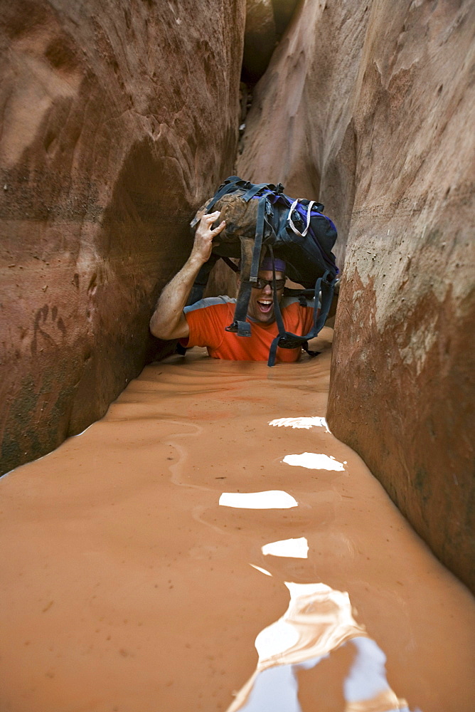 A man wading through water in narrow canyon, Utah.