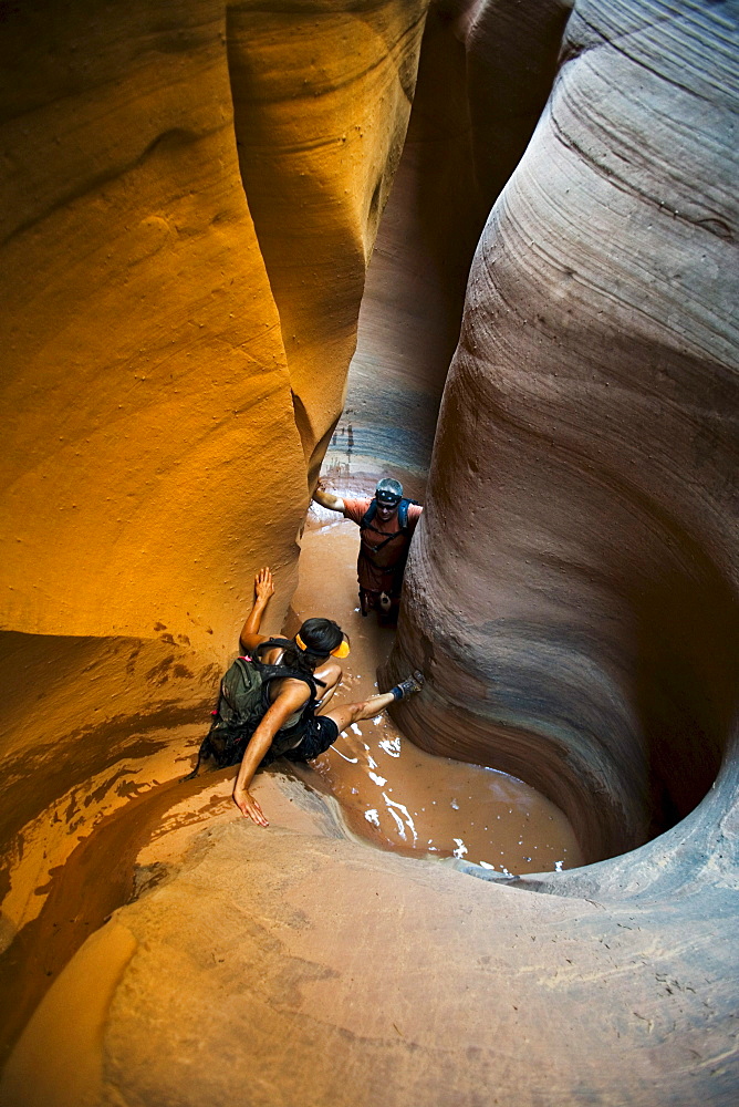 A woman down climbing into pool with man in pool in sculpted slot canyon, Utah.