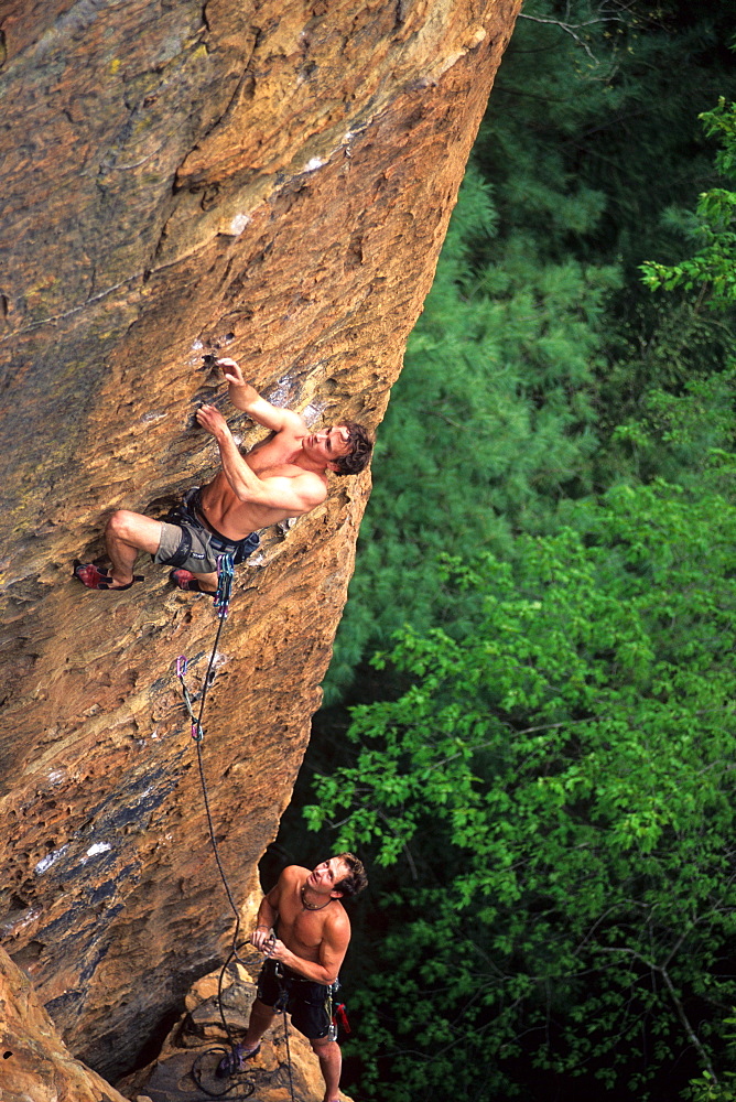 Two men rock climbing on sandstone in a Kentucky forest.