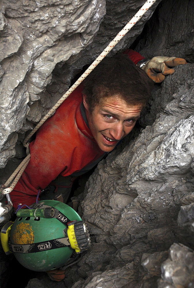 A cave explorer has to remove his helmet in order to pass the tight squeeze in an entrance to a cave in the White Mountains on t