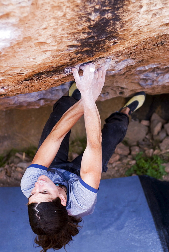 A young woman pulls hard on the small holds of Cholos, a V9 at the Happy Boulders near Bishop, California.