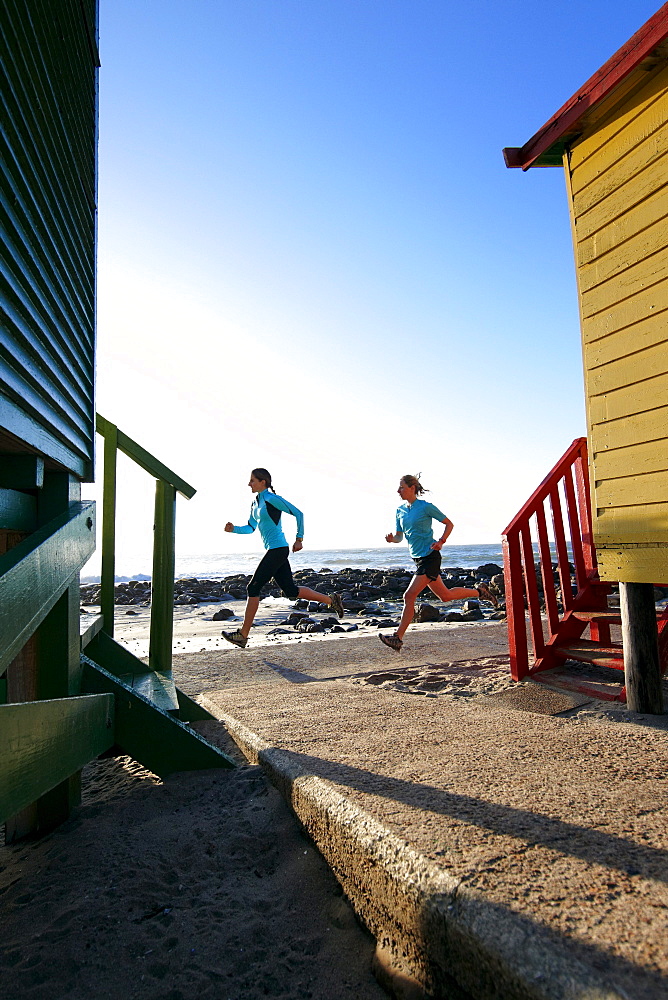 Katrin Schneider and Susann Scheller running past the famous and colorful bathing huts in St.James near Muizenberg. Cape Town, South Africa.