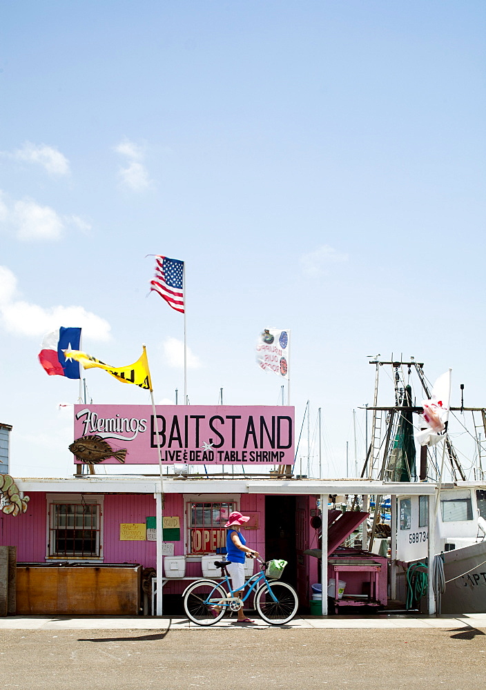 ROCKPORT, TEXAS, USA. A woman walks her bike in front of a bait stand in a small coastal town.