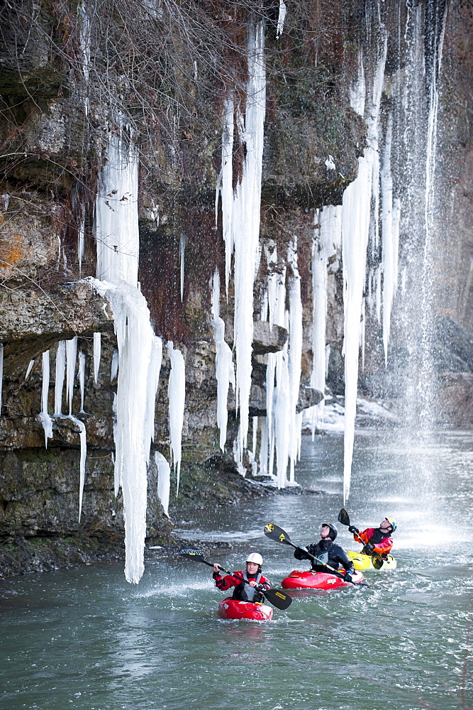 Three professional kayakers paddle under large icicles in Tennessee.