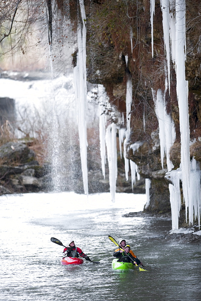 Three professional kayakers paddle under large icicles in Tennessee.