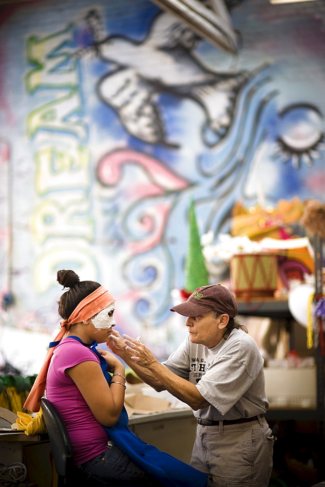 A woman creates a mask on a girl for a parade in Santa Barbara. The parade features extravagant floats and costumes.