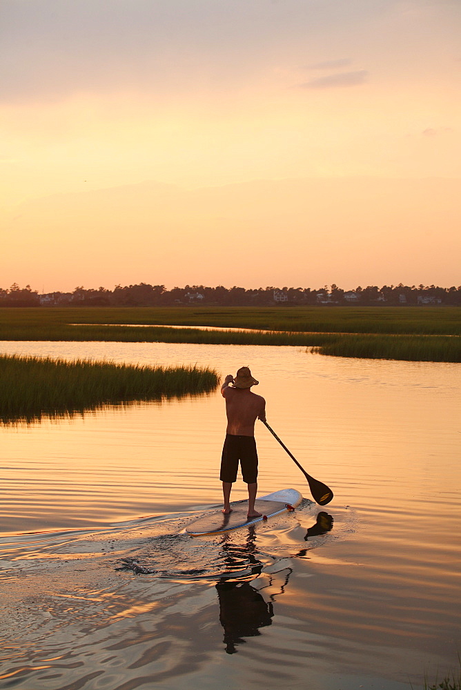 A man stand up paddle boarding in the Marsh